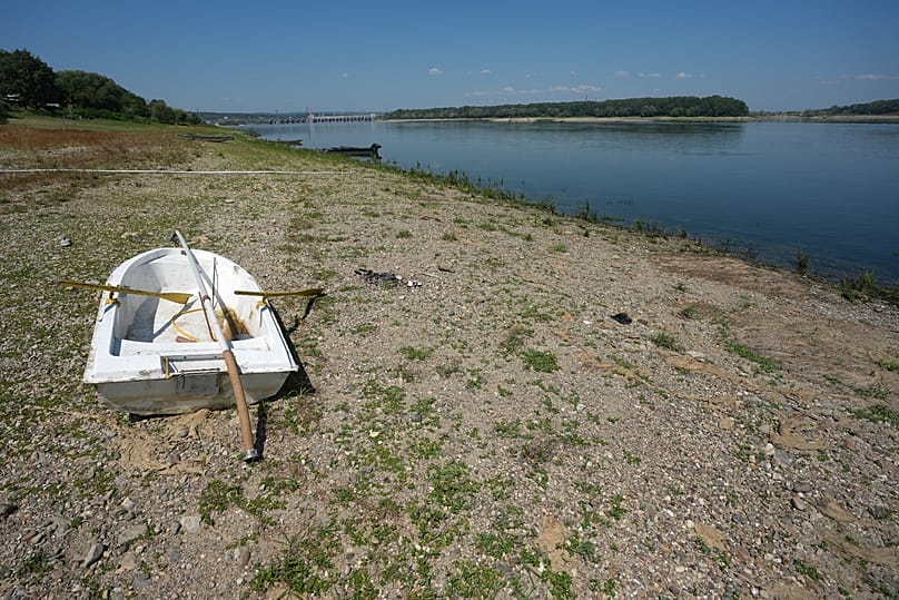 A boat laying on a dry bank in front of Djerdap II, a large dam on the Danube River, between Romania and Serbia, near Prahovo, Serbia, Tuesday, Aug. 4, 2026.