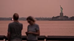A Estátua da Liberdade vê-se através da névoa causada pelo fumo dos incêndios no Canadá, ao pôr do sol de 5 de agosto de 2025, em Nova Iorque.
