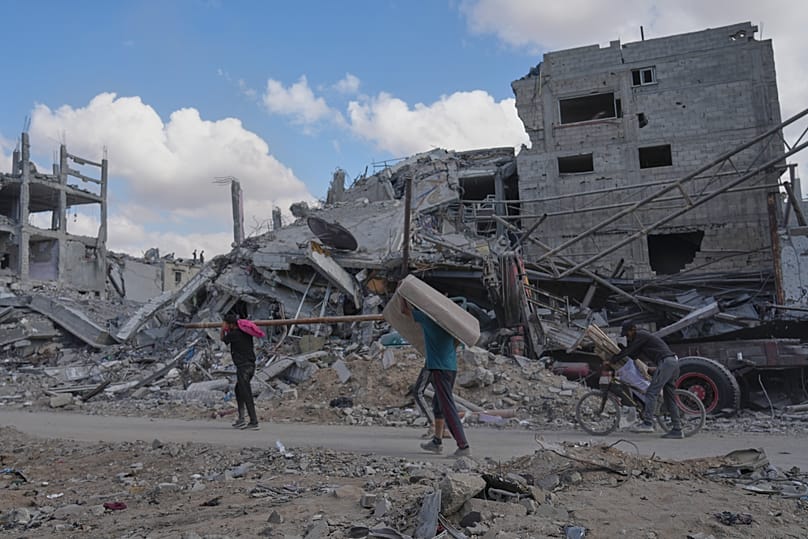 فلسطينيون يحملون أمتعتهم بين المباني المدمرة في مدينة غزة، 12 أكتوبر 2025، بعد الاتفاق على وقف القتال.
