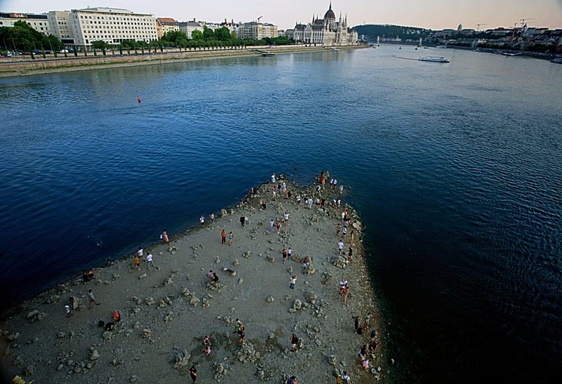 People walk on a sandbar underneath the Danube's Margareth Bridge in downtown Budapest, Hungary, Wednesday 5 August 2026, as the river hits never-before-seen low water levels.