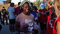 Migrantes que atravessaram de Marrocos para Espanha fazem fila para receber comida numa praia do enclave espanhol de Ceuta, segunda-feira, 3 de agosto de 2026