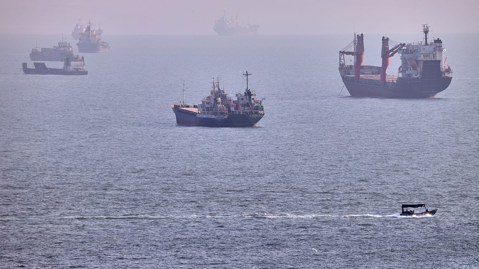 FILE: A small boat sails past cargo ships and other commercial vessels anchored in the Strait of Hormuz off Bandar Abbas, 5 August 2026