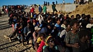 Migrants who crossed from Morocco into Spain line up for food distribution on a beach in the Spanish enclave of Ceuta, 3 August, 2026