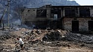 Человек тянет отсоединённый высоковольтный кабель перед сгоревшим зданием после лесного пожара в Круе, к северу от Тираны, Албания, в воскресенье 9 августа 2026 года