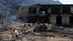 Uma pessoa puxa um cabo elétrico de alta tensão junto a um edifício incendiado após incêndio florestal em Krujë, a norte de Tirana, na Albânia, 9 de agosto de 2026