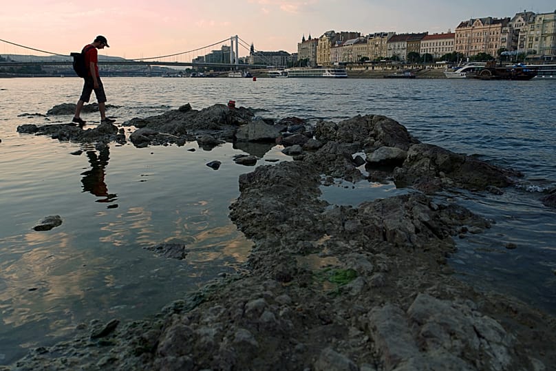 A man walks on rocks peeking out of the Danube, with critical low water levels, in downtown Budapest, Hungary, Wednesday Aug. 5, 2026.