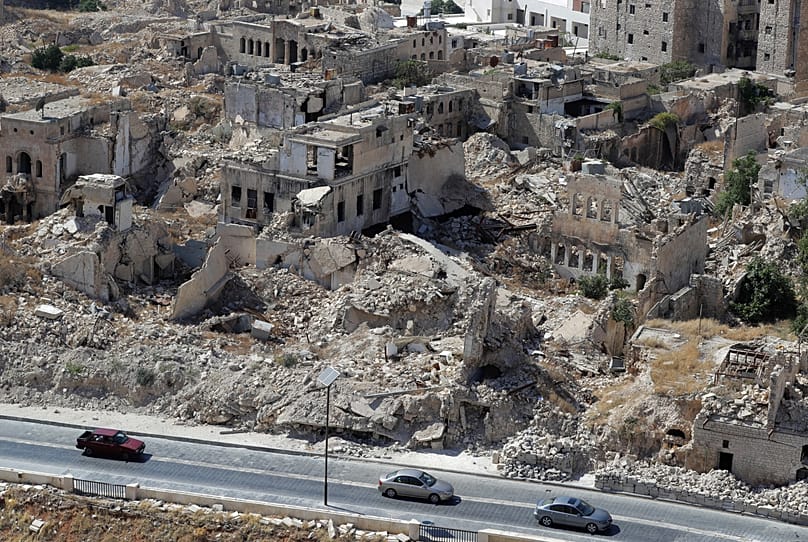 FILE: People drive their cars past destroyed buildings in the city of Aleppo, 16 August 2018