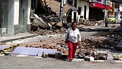 Kobieta idzie ulicą zasypaną gruzem dzień po trzęsieniu ziemi.