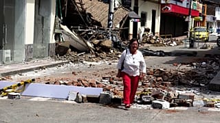 Une femme marche dans une rue jonchée de débris, un jour après le séisme