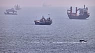 A small boat sails past cargo ships and other commercial vessels anchored in the Strait of Hormuz off Bandar Abbas, Iran, 5 Aug. 2026
