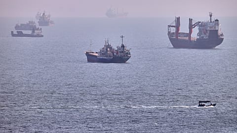 A small boat sails past cargo ships and other commercial vessels anchored in the Strait of Hormuz off Bandar Abbas, Iran, 5 Aug. 2026