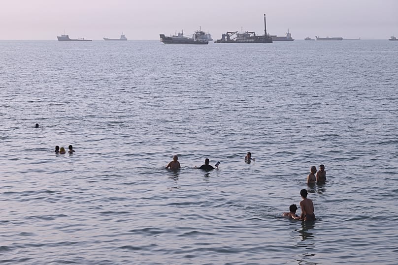 Residents swim as cargo and commercial vessels are anchored in the Strait of Hormuz off Bandar Abbas, 6 August, 2026