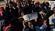 A migrant who crossed from Morocco to Spain holds a sign reading "asilo" in Spanish as he queues for food on a beach in the Spanish enclave of Ceuta