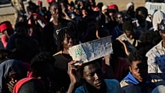 A migrant who crossed from Morocco to Spain holds a sign reading "asilo" in Spanish as he queues for food on a beach in the Spanish enclave of Ceuta