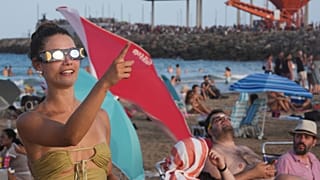 Valensiya yakınlarındaki Puerto de Sagunto sahilinde, özel tutulma gözlüğü takan bir plaj sakini, güneş tutulmasının kısmi evresi başlamadan göğe işaret ediyor.