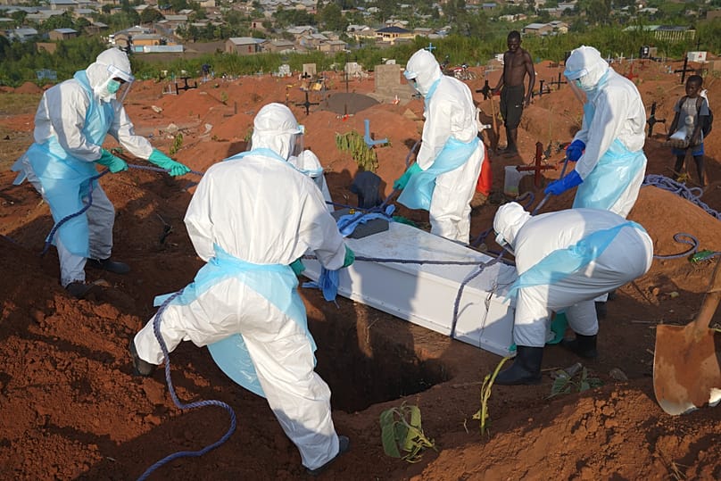 People in protective gear lower into a grave the coffin containing the remains of Jacques Lobo Dhena, who died of Ebola, during a burial service in Bunia, Ituri province, DRC.