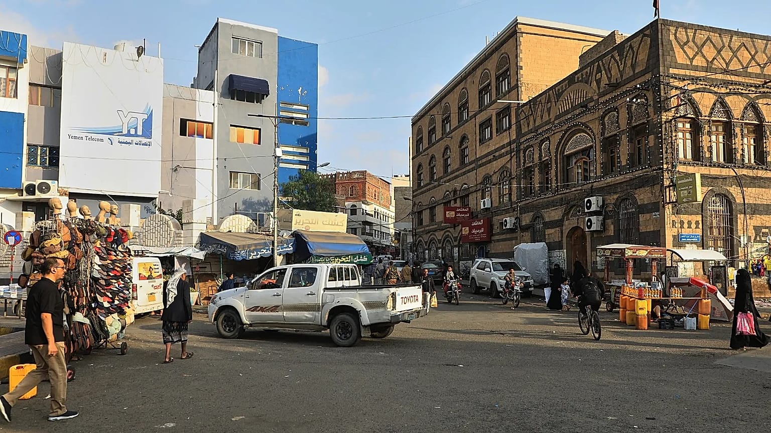 Varias personas pasan junto a vendedores de mercancías en una calle de Saná, Yemen, el sábado ocho de agosto de 2026. (Foto AP/Osamah Abdulrahman)