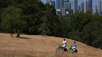 Des personnes font du vélo dans Greenwich Park, au milieu de l'herbe desséchée, à Londres, le mardi 11 août 2026.