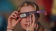 A person observes a partial solar eclipse with special protective glasses at Crosby beach in Liverpool as the moon covers part of the sun in Liverpool, England
