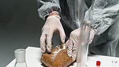 Pracownik laboratorium analizuje sproszkowaną substancję w laboratorium, korzystając ze sprzętu ochronnego.