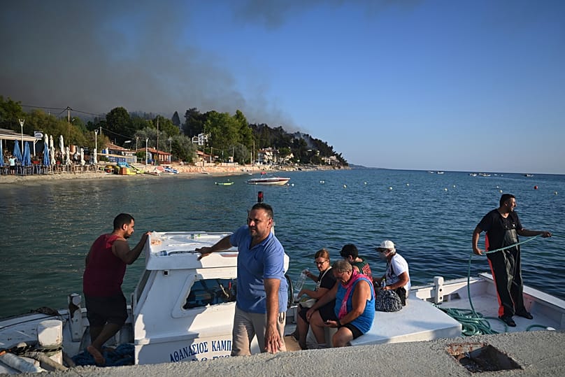 Tourists are evacuated by a fishing boat during a wildfire in Siviri, 13 August, 2026