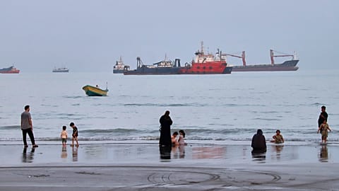 People on the beach as commercial vessels are anchored in the Strait of Hormuz off Bandar Abbas, 5 August, 2026