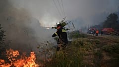 A volunteer firefighter uses a tree branch to extinguish flames during a wildfire in Siviri, 13 August, 2026