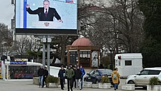 People walk in front of a screen showing Russian President Vladimir Putin during his annual state of the nation address in Sevastopol, 21 February, 2023