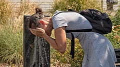 Uma mulher refresca o rosto numa fonte pública num dia de calor em Bordéus, França, quinta-feira, 13 de agosto de 2026, durante uma onda de calor no país