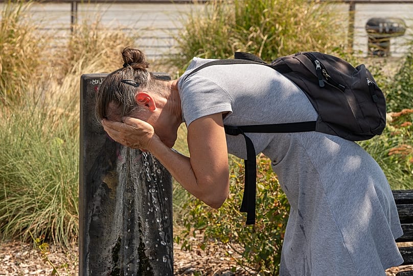 A woman splashes water on her face at a public fountain on a hot day in Bordeaux, 13 August, 2026