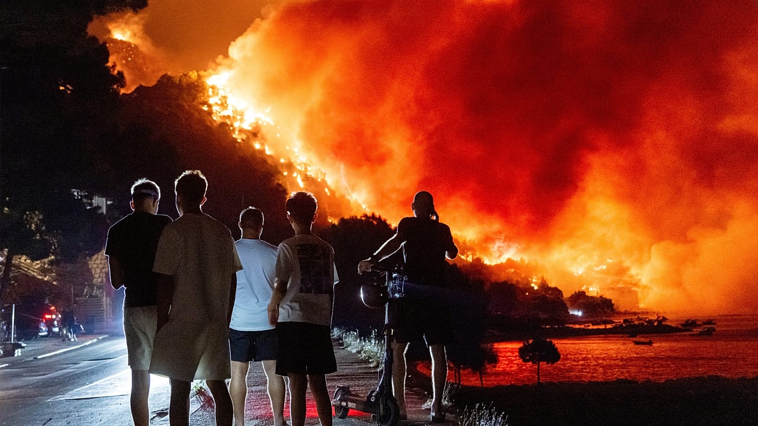 Varias personas observan un incendio forestal en la costa adriática cerca de Omis, en el sur de Croacia, la madrugada del viernes 14 de agosto de 2026.