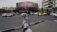 امرأة تسير في شارع بطهران، بينما تظهر خلفها لوحة لتمثال الحرية ساقطاً وحشود تحمل أعلاماً إيرانية، في ميدان الثورة.