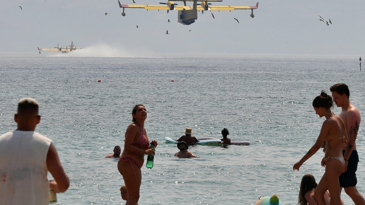 Bañistas observan los aviones contra incendios que recogen agua del Adriático durante un incendio forestal cerca de Omis