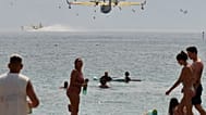 Beachgoers look at the firefighting airplanes scooping water from the Adriatic Sea during a wildfire near Omis
