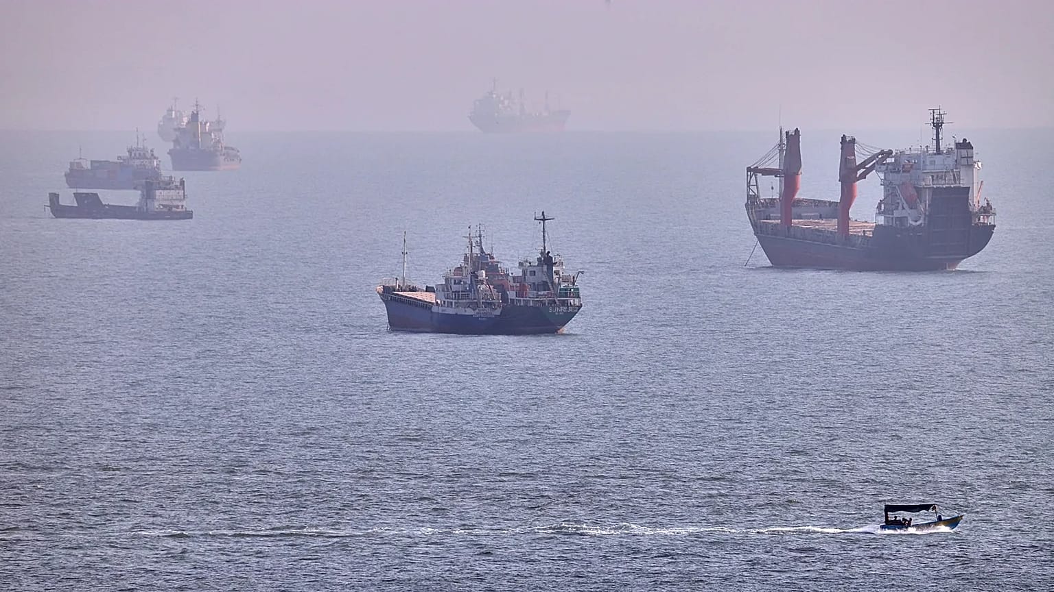 A small boat sails past cargo ships and other commercial vessels anchored in the Strait of Hormuz off Bandar Abbas, Iran, Wednesday, Aug. 5, 2026.