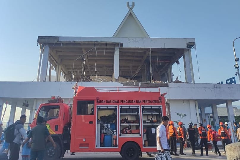 People walk past a building damaged during an earthquake in Maumere, East Nusa Tenggara province