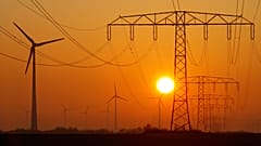 Nap kel fel az elektromos vezetékeket tartó oszlopok és szélturbinák mögött a Berlinhez közeli Nauenben, Németországban.