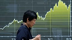 Osoba idzie przed elektroniczną tablicą z wykresem indeksu Nikkei w tokijskim biurze maklerskim, 13 sierpnia 2026 r.