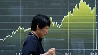 A person walks in front of an electronic stock chart board showing Japan's Nikkei index at a securities firm in Tokyo, 13 Aug. 2026