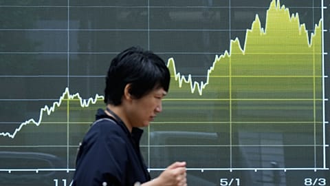 A person walks in front of an electronic stock chart board showing Japan's Nikkei index at a securities firm in Tokyo, 13 Aug. 2026