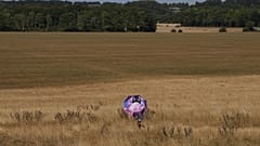 Osoba z parasolem idzie przez suchą trawę w Stonehenge w hrabstwie Wiltshire w Anglii, w czwartek 13 sierpnia 2026 r. (AP Photo/Kin Cheung)