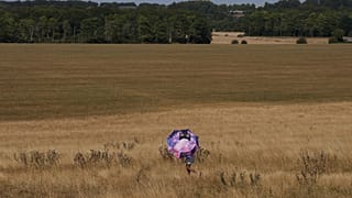 A person holds an umbrella and walks through dry grass at Stonehenge in Wiltshire, England, Thursday, Aug. 13, 2026. (AP Photo/Kin Cheung)