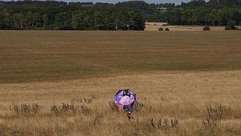 A person holds an umbrella and walks through dry grass at Stonehenge in Wiltshire, England, Thursday, Aug. 13, 2026. (AP Photo/Kin Cheung)