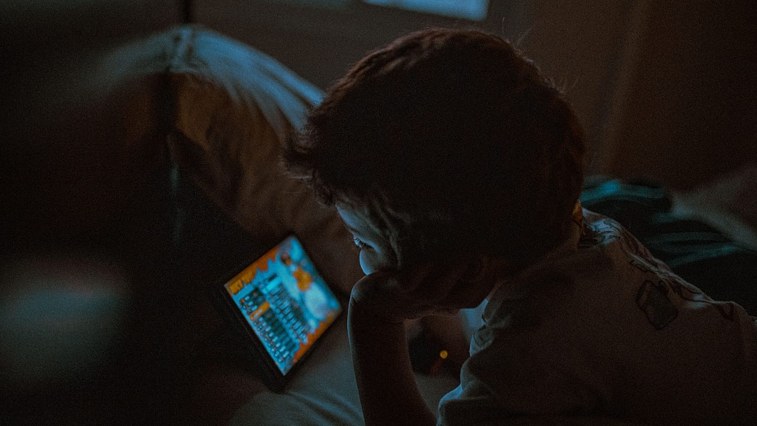 Ein kleines Kind schaut nachts auf ein Tablet.