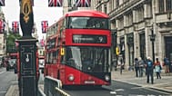 Iconic red double-decker bus on a busy street in London, England, with British flags overhead.
