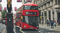 Iconic red double-decker bus on a busy street in London, England, with British flags overhead.