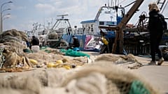 Fishermen mend nets in front of fishing boats at harbor in the Roman port of Fiumicino, 11 March, 2022.