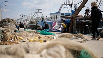 Fishermen mend nets in front of fishing boats at harbor in the Roman port of Fiumicino, 11 March, 2022.