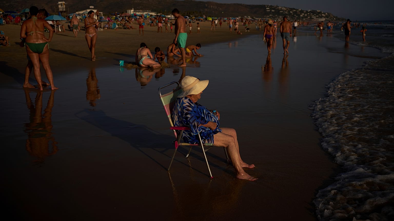 Una mujer se sienta en una silla mientras el sol se pone en la playa de Zahara de los Atunes en Cádiz, España, el jueves 13 de agosto de 2026
