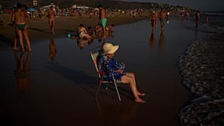 Una mujer se sienta en una silla mientras el sol se pone en la playa de Zahara de los Atunes en Cádiz, España, el jueves 13 de agosto de 2026